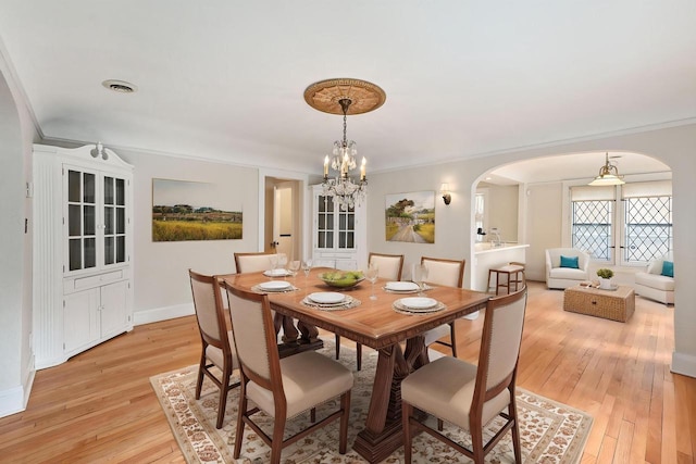dining room with crown molding, a notable chandelier, arched walkways, light wood-style flooring, and baseboards