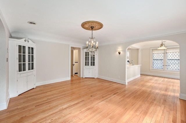 interior space featuring crown molding, arched walkways, baseboards, a notable chandelier, and light wood-style flooring