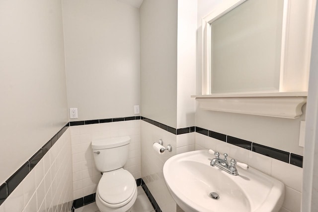 bathroom featuring a sink, wainscoting, toilet, and tile walls