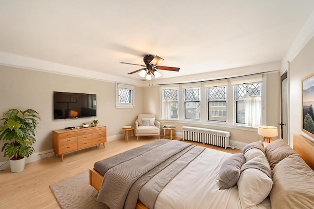 bedroom with radiator, baseboards, a ceiling fan, and light wood-type flooring