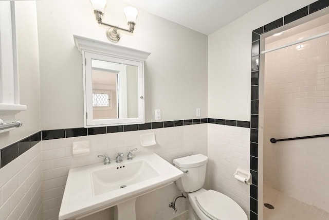 full bathroom featuring toilet, tile walls, tiled shower, and a wainscoted wall