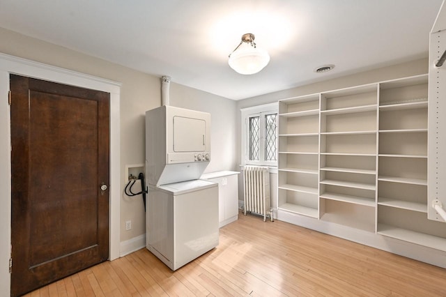 laundry room featuring stacked washer and dryer, laundry area, light wood finished floors, radiator, and visible vents