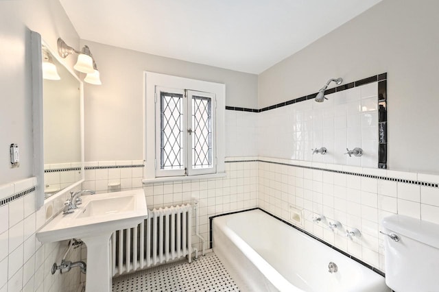 bathroom featuring tile walls, wainscoting, a bathing tub, toilet, and radiator heating unit
