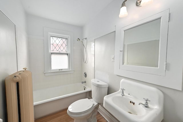 bathroom with a sink, bathtub / shower combination, toilet, radiator heating unit, and wood finished floors