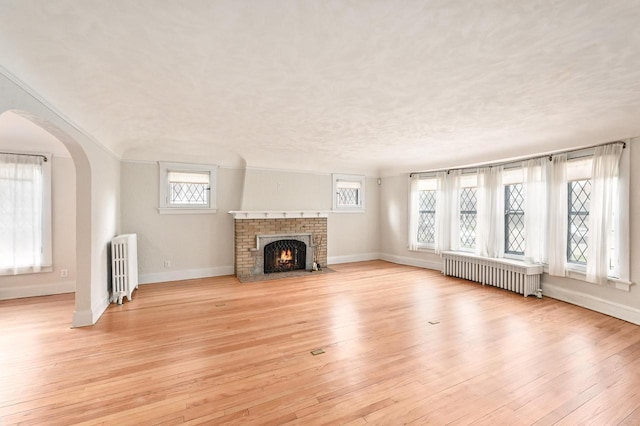 unfurnished living room featuring radiator heating unit, baseboards, and light wood-style floors