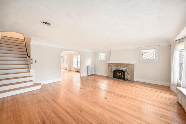 unfurnished living room featuring a brick fireplace, light wood-style flooring, baseboards, visible vents, and stairway