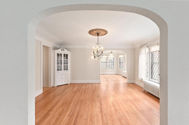 unfurnished dining area with light wood-style floors, arched walkways, a chandelier, radiator, and baseboards