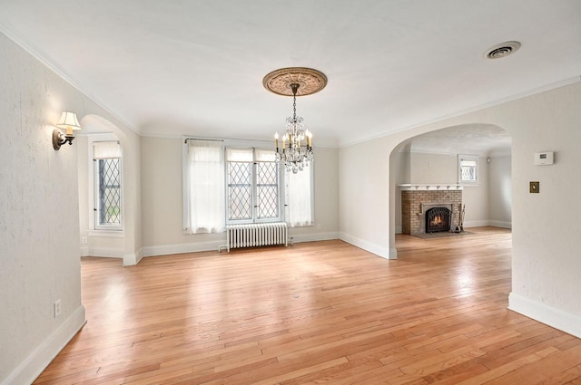 unfurnished dining area featuring an inviting chandelier, ornamental molding, a brick fireplace, and radiator heating unit
