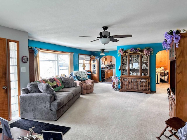 living area featuring arched walkways, ceiling fan, carpet, and a textured ceiling