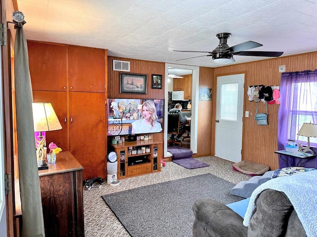 carpeted living area with a ceiling fan, wood walls, and visible vents