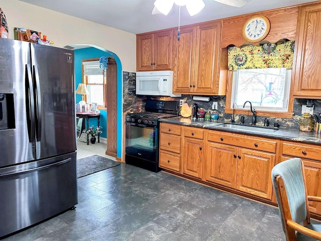 kitchen with white microwave, stainless steel fridge, arched walkways, a sink, and gas stove