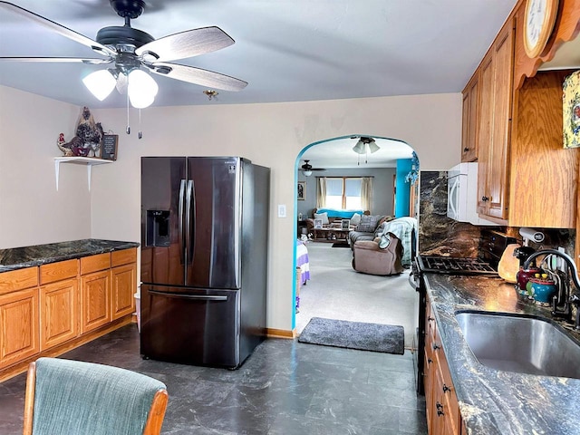 kitchen featuring ceiling fan, brown cabinetry, arched walkways, a sink, and black fridge