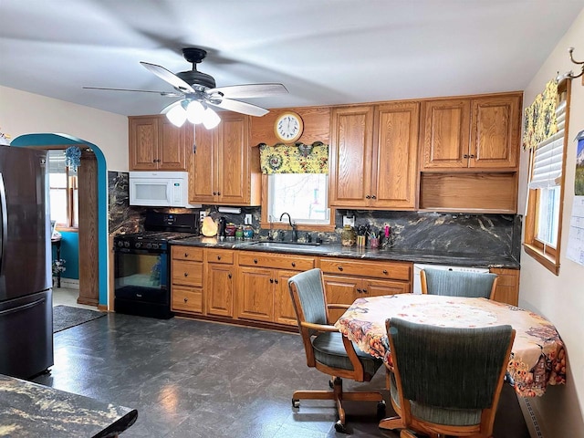 kitchen with black gas range, freestanding refrigerator, decorative backsplash, white microwave, and a sink