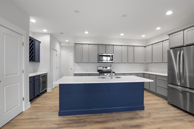 223 NW 3rd Ave, Monroe, WI 53566 - kitchen featuring a kitchen island with sink, a sink, light wood finished floors, beverage cooler, and stainless steel appliances