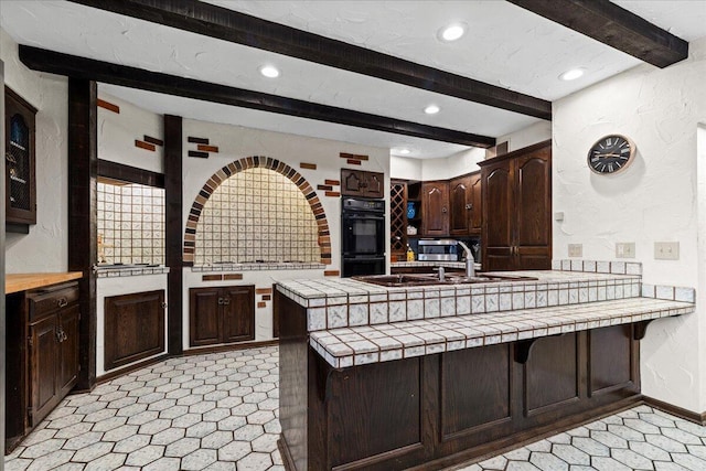 N84W16033 Menomonee Ave Unit 200, Menomonee Falls, WI 53051 - kitchen featuring beamed ceiling, dark brown cabinetry, a peninsula, tile counters, and recessed lighting
