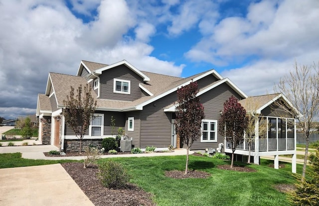 view of front facade featuring driveway, central AC unit, a sunroom, a front lawn, and a shingled roof