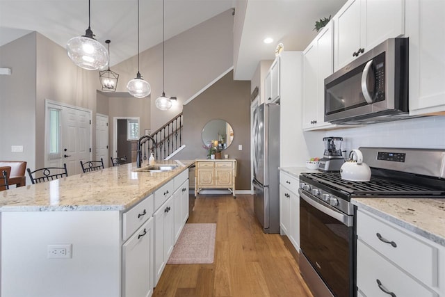 kitchen featuring a sink, stainless steel appliances, a center island with sink, white cabinets, and light wood-style floors