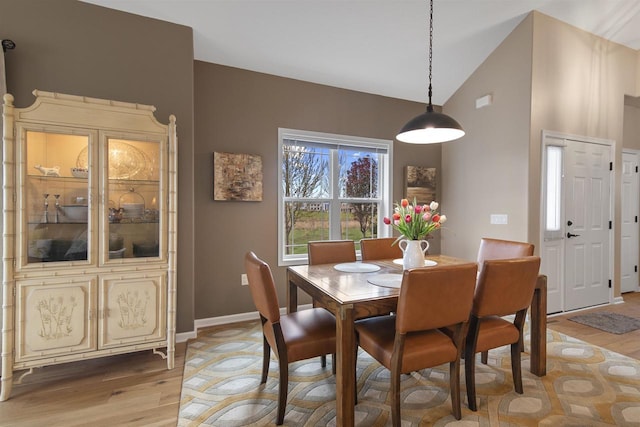 dining room featuring light wood-style flooring, baseboards, and high vaulted ceiling