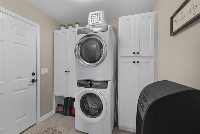 clothes washing area with stacked washer and clothes dryer, cabinet space, and baseboards