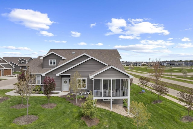 view of front of property with roof with shingles, a sunroom, and a front yard