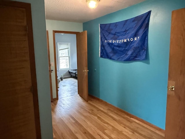 hall with baseboards, a textured ceiling, and wood finished floors