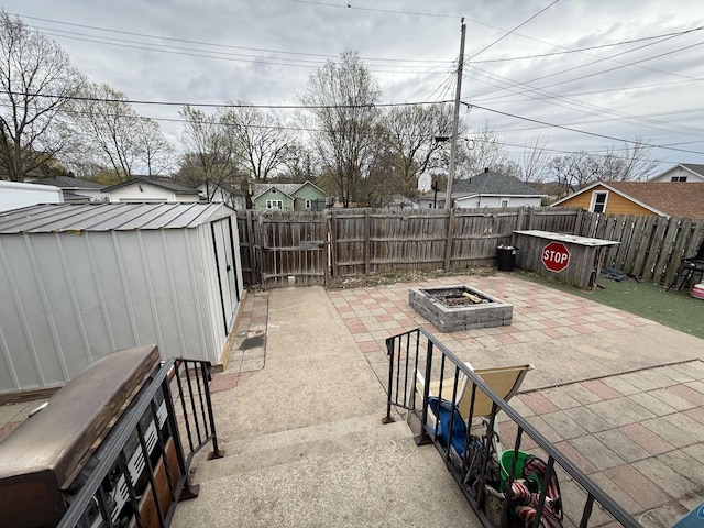 view of patio / terrace featuring a fenced backyard, a storage unit, an outdoor structure, and a fire pit