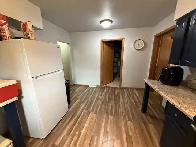kitchen featuring dark cabinetry, freestanding refrigerator, wood finished floors, and light countertops