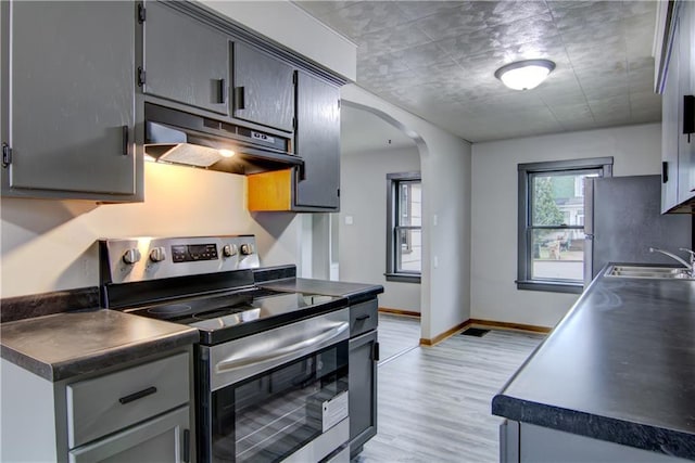 208 W Grand Ave, Chippewa Falls, WI 54729 - kitchen featuring arched walkways, under cabinet range hood, a sink, light wood finished floors, and appliances with stainless steel finishes