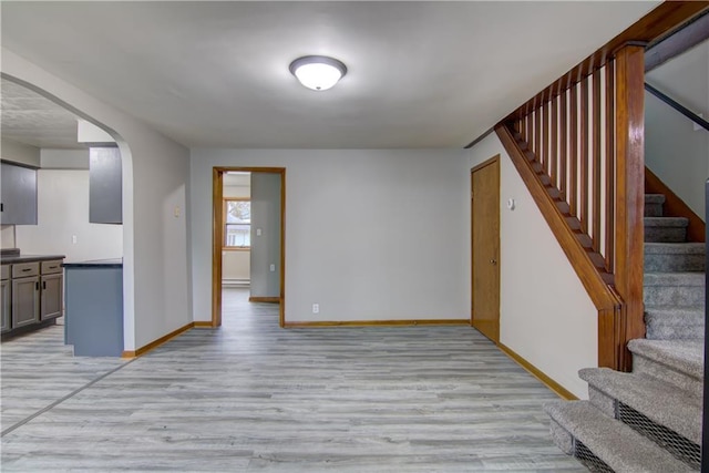 208 W Grand Ave, Chippewa Falls, WI 54729 - unfurnished living room with arched walkways, baseboards, light wood finished floors, and stairs