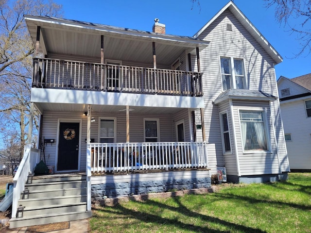 view of front facade featuring a porch, a chimney, a balcony, and a front lawn