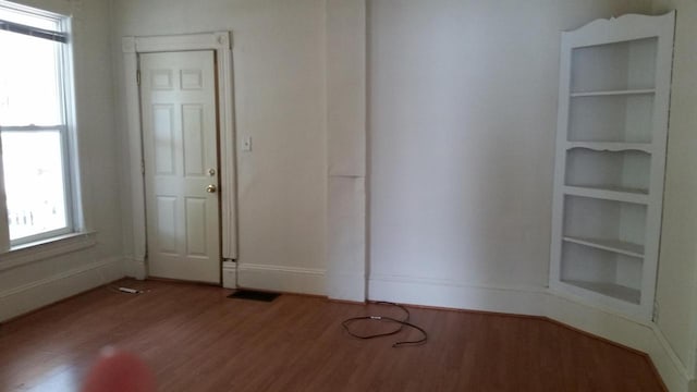 unfurnished room with baseboards, plenty of natural light, wood finished floors, and visible vents