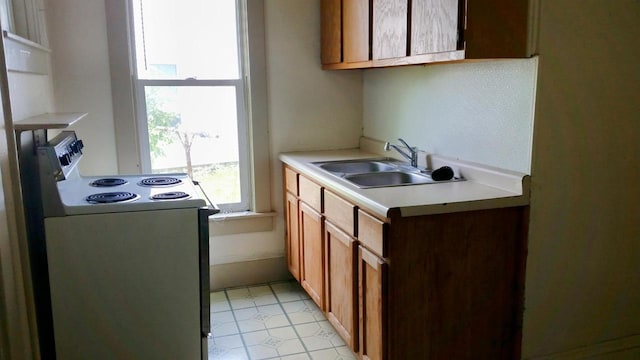kitchen with brown cabinetry, a sink, range with electric cooktop, and light countertops