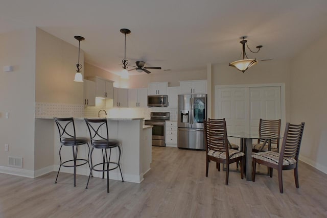 kitchen with visible vents, tasteful backsplash, light wood finished floors, a peninsula, and stainless steel appliances