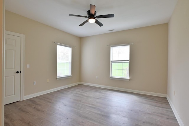 empty room featuring plenty of natural light, baseboards, wood finished floors, and visible vents