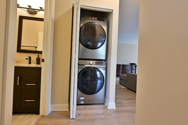 washroom with stacked washer / drying machine, laundry area, a sink, and light wood finished floors