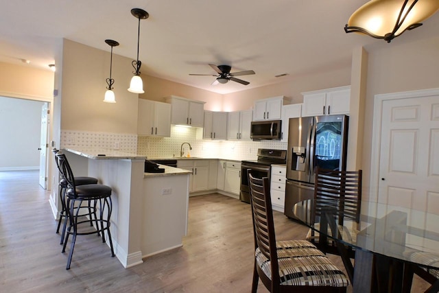 kitchen featuring decorative backsplash, a ceiling fan, a peninsula, light wood-style floors, and stainless steel appliances