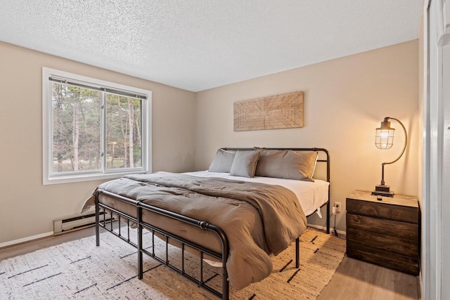 bedroom featuring a textured ceiling, baseboards, a baseboard heating unit, and light wood finished floors