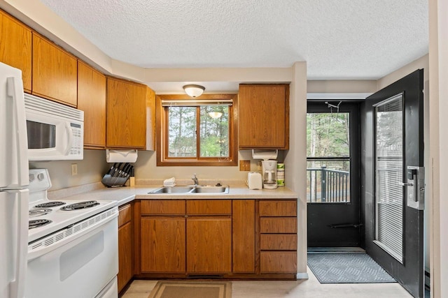 kitchen with a sink, plenty of natural light, white appliances, and a textured ceiling
