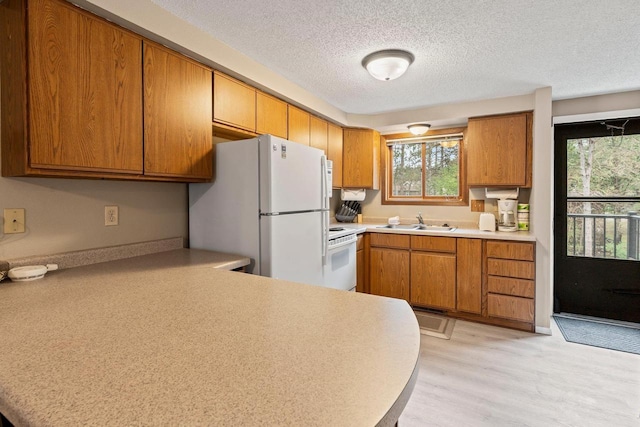 kitchen featuring a sink, light countertops, freestanding refrigerator, and brown cabinetry