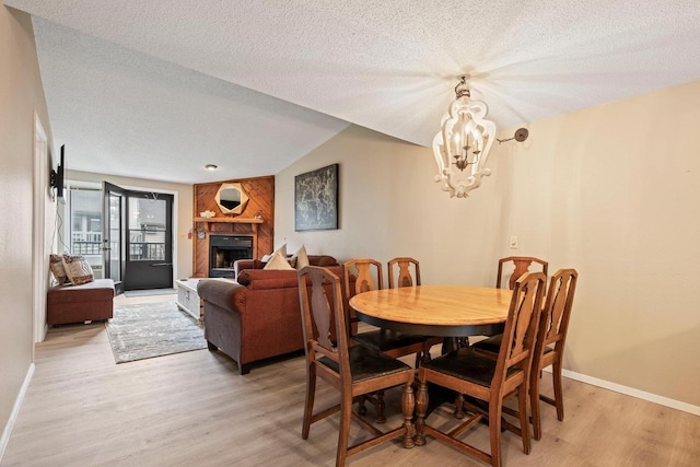 dining area featuring an inviting chandelier, a fireplace, baseboards, a textured ceiling, and light wood-style flooring