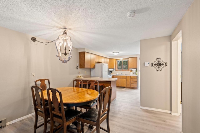 dining area with a textured ceiling, baseboards, a notable chandelier, and light wood-type flooring