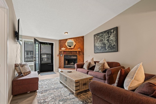 living area with a fireplace with raised hearth, a textured ceiling, and wood finished floors