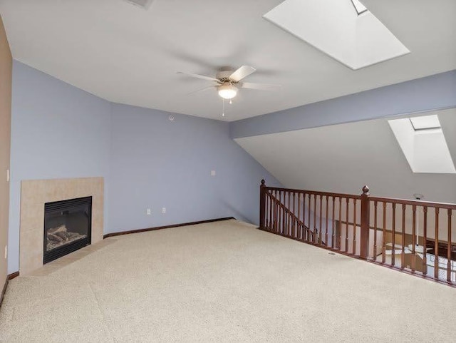 bonus room with ceiling fan, a skylight, a tiled fireplace, baseboards, and carpet flooring