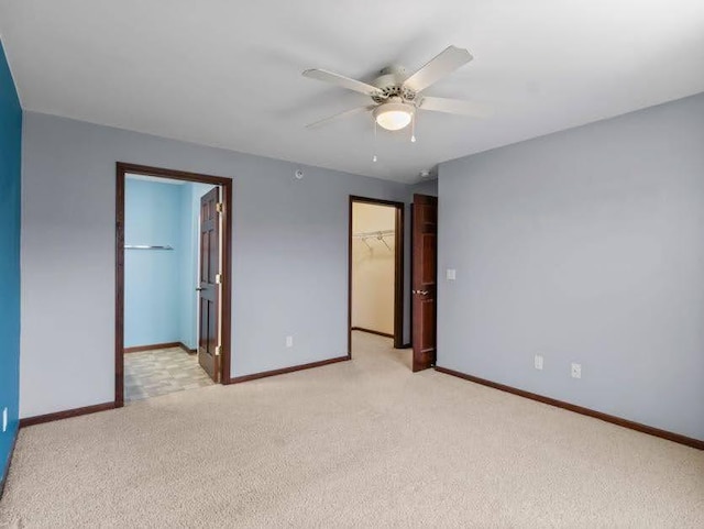 unfurnished bedroom with ceiling fan, light colored carpet, a walk in closet, baseboards, and a closet