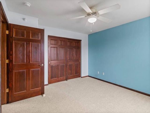unfurnished bedroom featuring baseboards, a ceiling fan, a closet, and light colored carpet