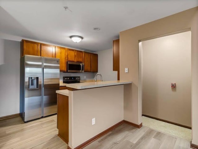 kitchen featuring brown cabinetry, appliances with stainless steel finishes, light wood-type flooring, light countertops, and a peninsula