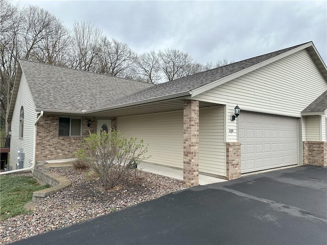 view of side of property featuring brick siding, an attached garage, roof with shingles, and driveway