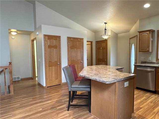 kitchen featuring a center island, stainless steel dishwasher, vaulted ceiling, light countertops, and light wood finished floors