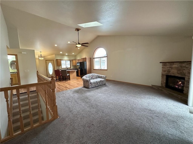 living area featuring light carpet, a fireplace, a ceiling fan, baseboards, and lofted ceiling with skylight