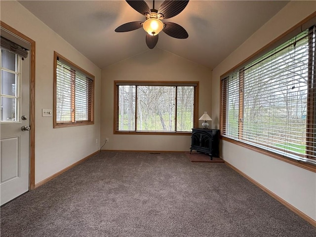 empty room with a wood stove, carpet, a wealth of natural light, and vaulted ceiling